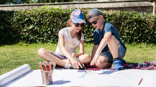 A boy and a girl sat on a country lawn enjoying a drawing activity in the sunshine.